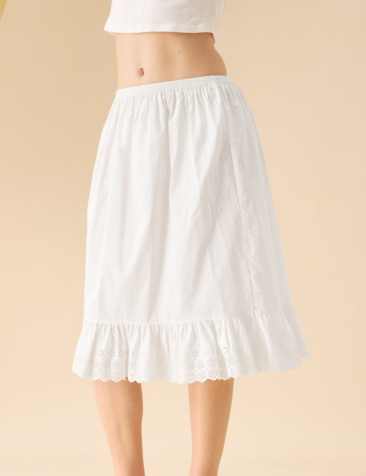 Mid-shot of a model wearing an Ivory mid-length cotton halfs lip featuring an elastic waistband and embroidered eyelet lace trim.