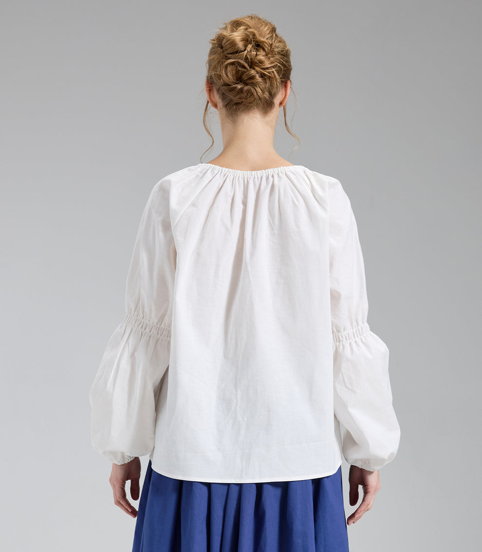Back view of an ivory peasant top displaying the gathered back neckline and elegant sleeve shirring details.