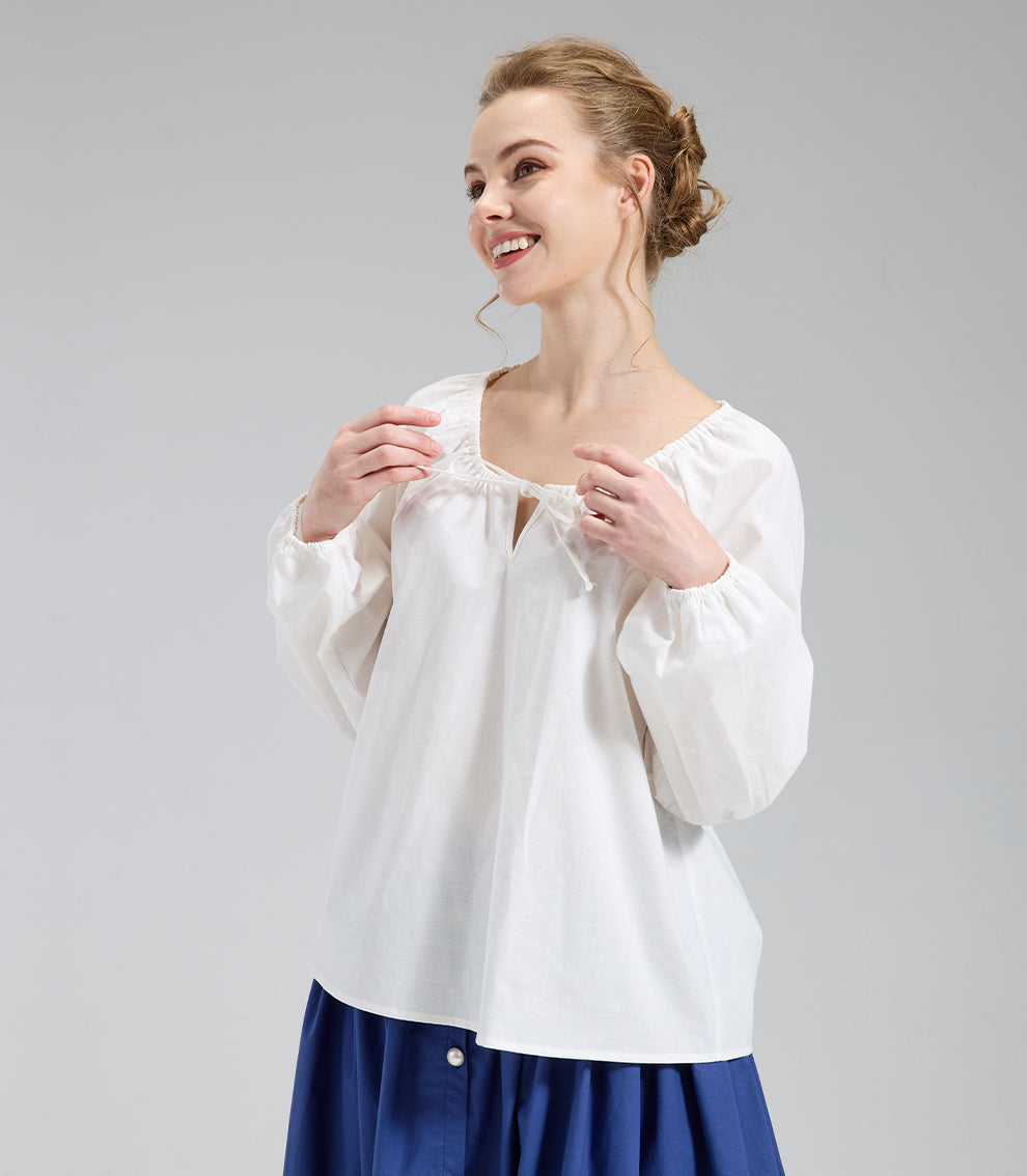 Model smiling and adjusting the drawstring detail on a romantic ivory boho blouse with voluminous sleeves.
